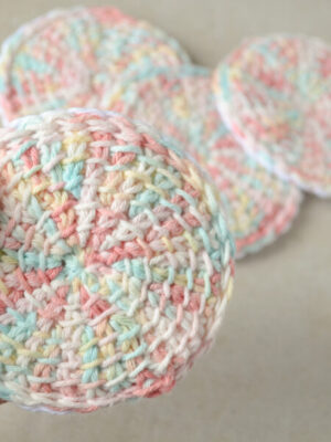 Front view of a Tunisian crochet face scrubby versus a pile of other scrubbies