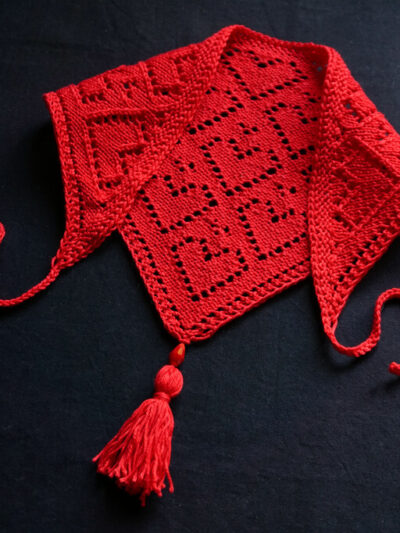 Knit bandana in red cotton yarn, with lace hearts motifs, ties and a tassel.