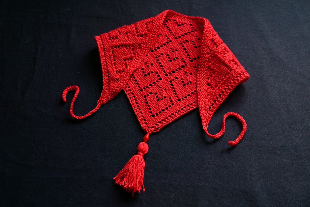 Knit bandana in red cotton yarn, with lace hearts motifs, ties and a tassel.