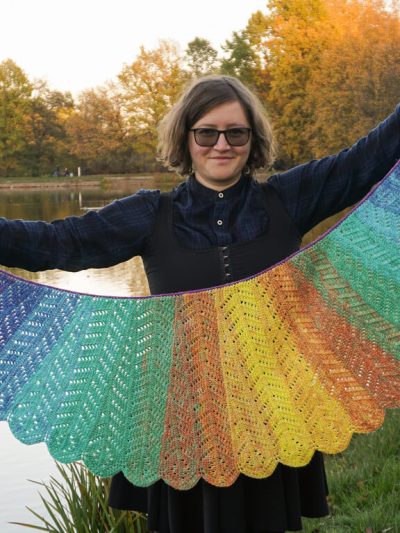 Macaw wings shawl spread out to show the different sized feathers, going from small purple ones, through larger dark blue, green, orange and yellow in the middle, back through the same progression towards the other end.