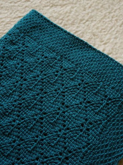 Folded dark green forest baby blanket with a lacy leaf motif and honeycomb border.