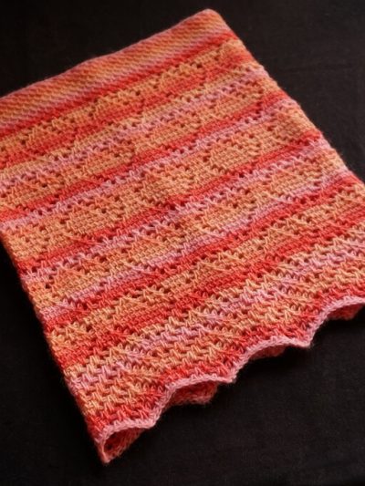 Peach grove cowl sample made in Tunisian crochet lace, with peach shaped lacy motifs, a wavy bottom edge and non-curling honeycomb border. Worked in sock yarn in shades of pink and peachy orange.